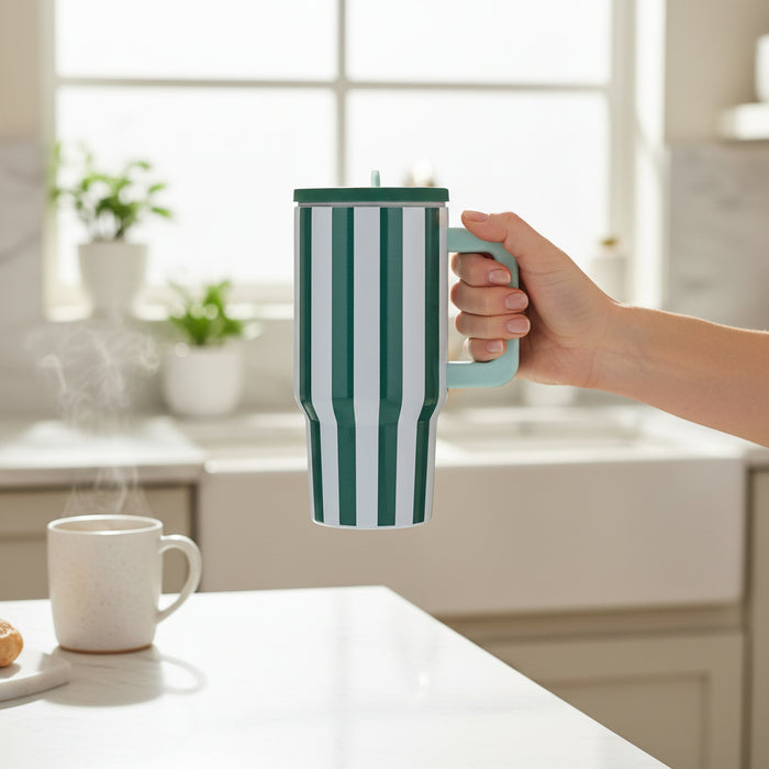 A hand holds The Darling Effect Sicily Stripes Teal 20 oz Lifestyle Flip Straw Tumbler in a bright kitchen, with an insulated tumbler, steaming white mug, and pastry on the counter as sunlight streams through the window.