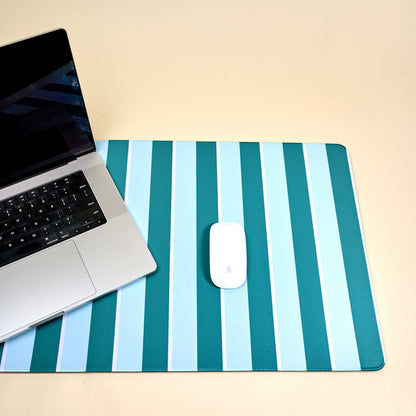 A silver laptop sits on the left side of The Darling Effect Sicily Stripes Teal Style Station Desk Mat, which features teal and light blue stripes and a non-slip base. A white Apple mouse rests securely on the mat.