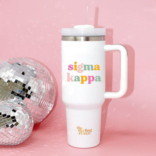 The Sigma Kappa 40 oz Take Me Everywhere White Tumbler by The Darling Effect, featuring “sigma kappa” in colorful letters and the brand’s logo, sits beside a silver disco ball on a pink background—making this insulated drinkware a fun and functional companion for all your adventures.