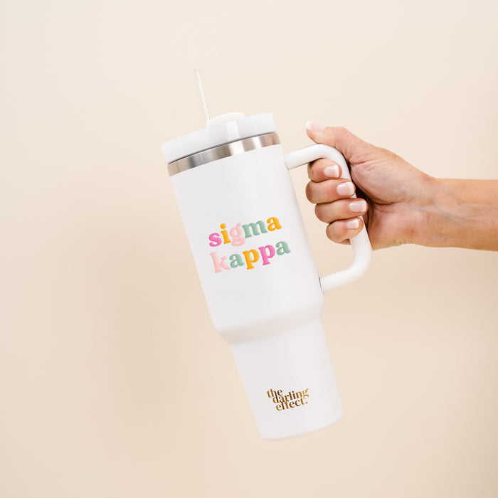 A hand holds The Darling Effect’s Sigma Kappa 40 oz Take Me Everywhere White Tumbler, featuring an easy-to-carry handle. This insulated drinkware showcases vibrant Sigma Kappa lettering and “The Uplifting Effect” near the base, while a white straw extends from the lid—making this tumbler both practical and eye-catching.