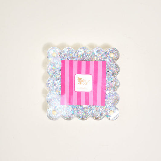 The Silver Glitter Little Moments Acrylic Picture Frame by The Darling Effect features a square, scalloped edge with glitter, a 2.5x2.5 photo space, pink and white striped insert, "the darling effect" text, and a magnetic closure.