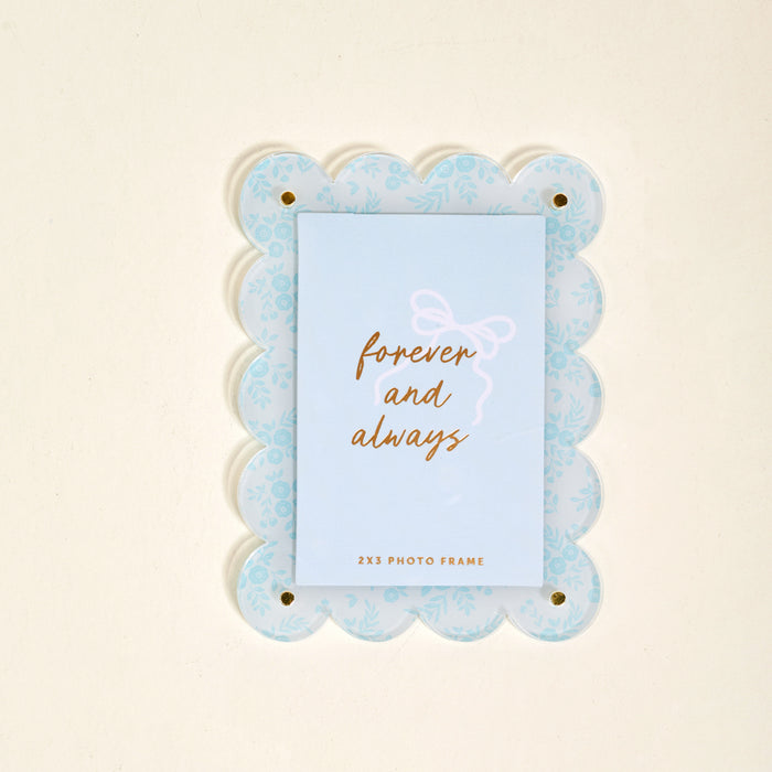 The Darling Effect’s Something Blue Mini Acrylic Picture Frame Magnet features a light blue scalloped design with a floral pattern and displays a card reading "forever and always" in gold script.