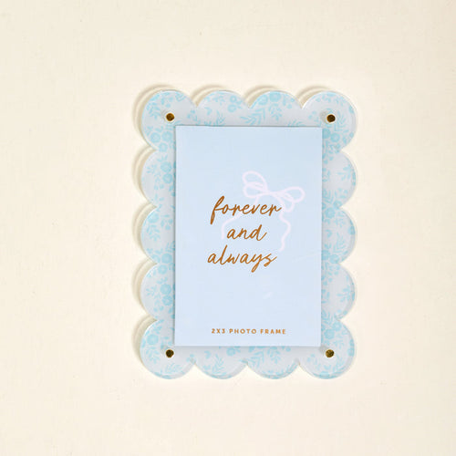 The Darling Effect’s Something Blue Mini Acrylic Picture Frame Magnet features a light blue scalloped design with a floral pattern and displays a card reading "forever and always" in gold script.