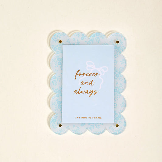The Darling Effect’s Something Blue Mini Acrylic Picture Frame Magnet features a light blue scalloped design with a floral pattern and displays a card reading "forever and always" in gold script.