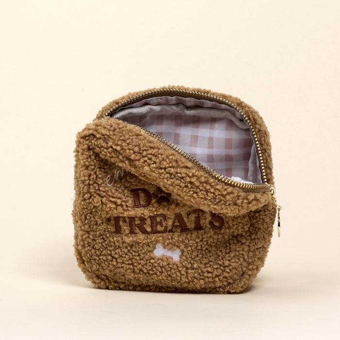 The Darling Effect's Square Emergency Dog Treats Teddy Pouch is a small, brown, square sherpa pouch with a gold zipper and checkered lining. "DOG TREATS" and a white bone are embroidered on the front.