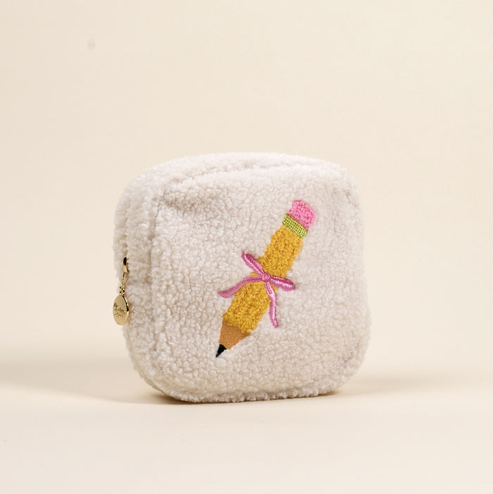 The Darling Effect’s Square Pencil Me In Teddy Pouch is a fuzzy white sherpa pouch featuring an embroidered yellow pencil with a pink eraser and tied with a pink ribbon.