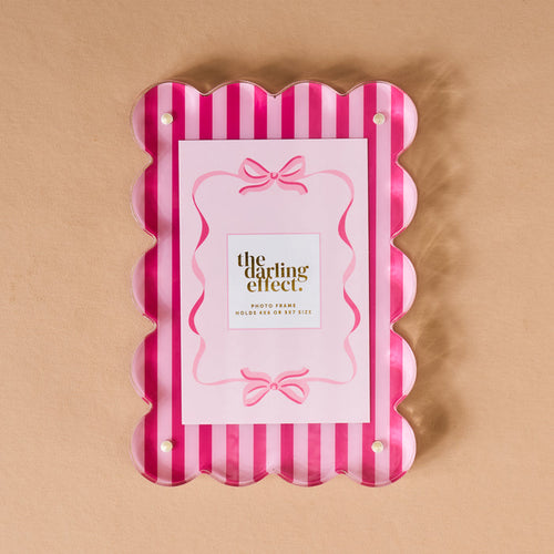 The Sweetheart Stripes Rectangle Scalloped Acrylic Frame by The Darling Effect features pink and white stripes, four visible screws, and is shown on a beige background with a placeholder card bordered by pink bows and gold “the darling effect” text.