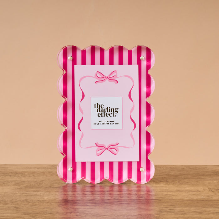 The Darling Effect’s Sweetheart Stripes Rectangle Scalloped Acrylic Frame, with pink and white vertical stripes and stylish scalloped edges, adds charm to any space.