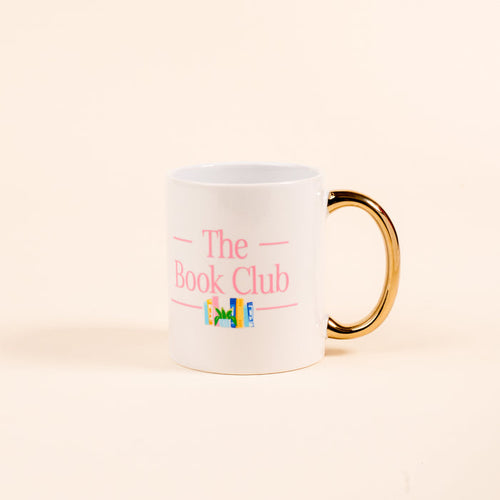 The Darling Effect’s The Book Club 11 oz Cozy Cute Ceramic Mug features a golden handle, pink "The Book Club" text, and colorful books beneath—perfect for sipping coffee or tea. Shown against a plain, light background.