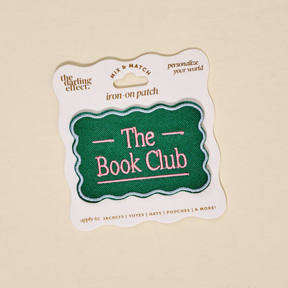 The Darling Effect’s The Book Club Mix & Match Iron-On Patch features a green scalloped edge and pink text, displayed on white packaging with gold and black details—ideal for customizing jackets, totes, hats, pouches, and more.