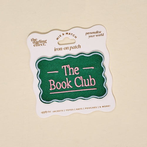 The Darling Effect’s The Book Club Mix & Match Iron-On Patch features a green scalloped edge and pink text, displayed on white packaging with gold and black details—ideal for customizing jackets, totes, hats, pouches, and more.