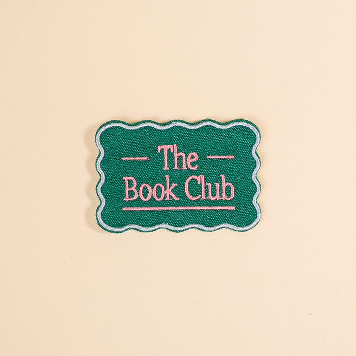 Customize your items with The Darling Effect’s The Book Club Mix & Match Iron-On Patch—a green patch with scalloped edges and pink “The Book Club” text, perfect for adding a colorful touch to any accessory.