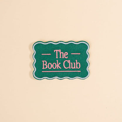 Customize your items with The Darling Effect’s The Book Club Mix & Match Iron-On Patch—a green patch with scalloped edges and pink “The Book Club” text, perfect for adding a colorful touch to any accessory.