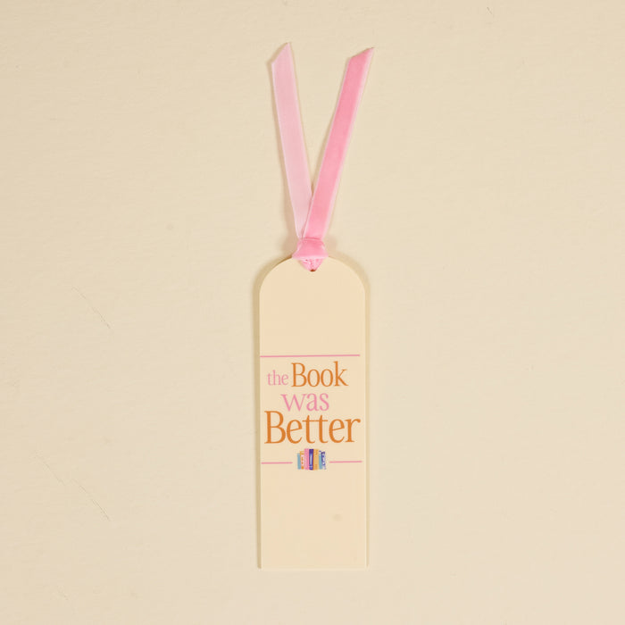 The Darling Effect’s "The Book Was Better" acrylic bookmark features cream coloring, a pink ribbon, pink and gold text, and a cute illustration of three colorful books at the bottom.