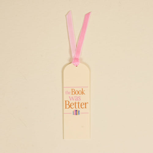 The Darling Effect’s "The Book Was Better" acrylic bookmark features cream coloring, a pink ribbon, pink and gold text, and a cute illustration of three colorful books at the bottom.