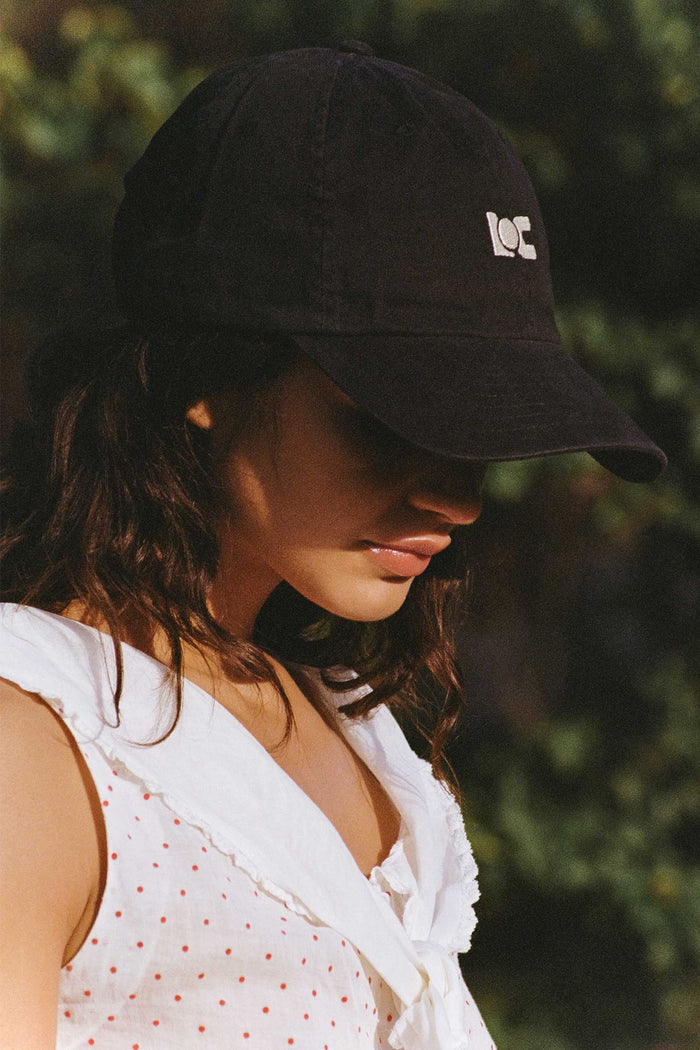 A woman wearing a black LOC cap with a logo, outdoors.