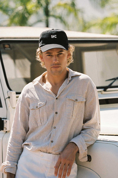 A model wearing the LOC Cap in washed black, leaning against a vehicle.
