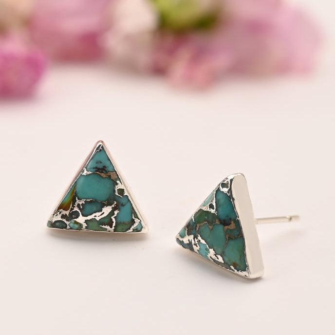 Triangle-shaped turquoise earrings on a light background with blurred pink flowers.