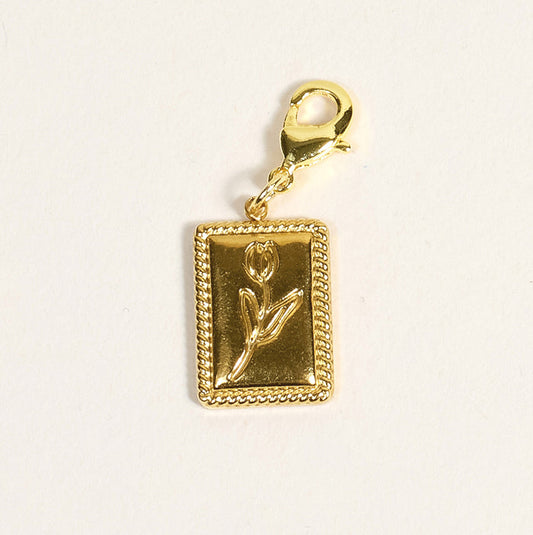 The Darling Effect's Tulip Time Jewelry Charm Gold features a raised tulip on a golden rectangular bar with a gold lobster clasp—ideal for adding a meaningful touch to your favorite charm jewelry.