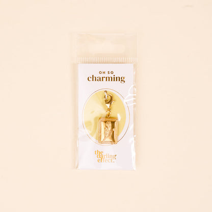 Add unique flair to your charm jewelry with the Tulip Time Jewelry Charm Gold by The Darling Effect—a gold-tone tulip in a rectangular frame on a lobster clasp. Comes in plastic packaging with “OH SO charming” and The Darling Effect branding.