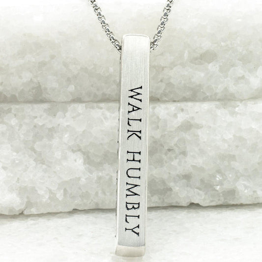 Silver necklace with a bar pendant engraved 'WALK HUMBLY' on a marble background