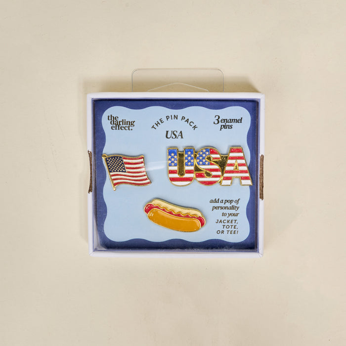 The Darling Effect’s USA The Pin Pack features three collectible pins—an American flag, USA in stars and stripes, and a hot dog—perfect for adding patriotic flair to your jacket, tote, or tee.