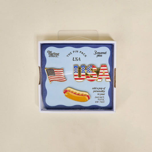 The Darling Effect’s USA The Pin Pack features three collectible pins—an American flag, USA in stars and stripes, and a hot dog—perfect for adding patriotic flair to your jacket, tote, or tee.