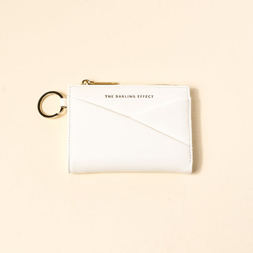 The Darling Effect White Luxe Pocket Wallet, made from vegan leather, features a gold zipper, key ring, and gold-printed logo on the front, shown on a light beige background.