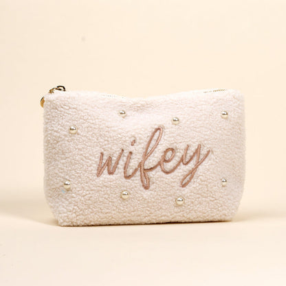 The Darling Effect Wifey & Pearls Teddy Pouch is a cream sherpa accessory, featuring embroidered "wifey" in script and scattered pearls—an adorable essential for any set.