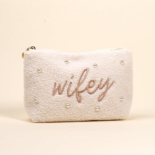 The Darling Effect Wifey & Pearls Teddy Pouch is a cream sherpa accessory, featuring embroidered "wifey" in script and scattered pearls—an adorable essential for any set.