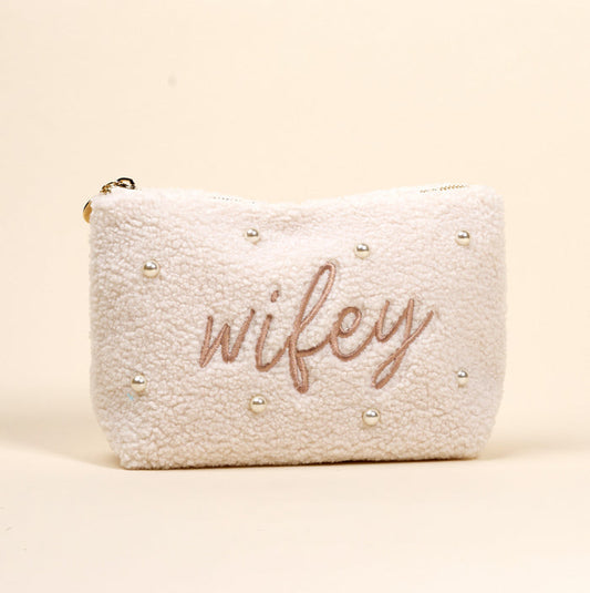 The Darling Effect Wifey & Pearls Teddy Pouch is a cream sherpa accessory, featuring embroidered "wifey" in script and scattered pearls—an adorable essential for any set.