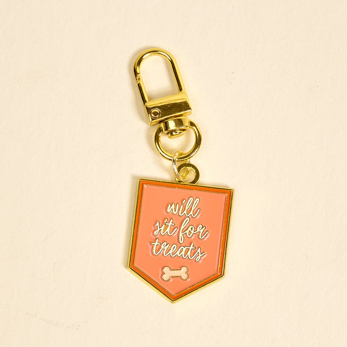 The Darling Effect’s Will Sit for Treats Pawfect Collar Charm features a gold keychain with a pink shield tag, white script, and bone icon—perfect for adding playful style to your pet accessories collection.