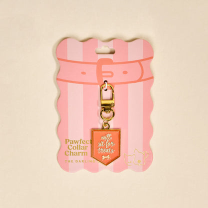 The Darling Effect's Will Sit for Treats Pawfect Collar Charm features gold and pink hues, a bone icon, and "will sit for treats" text on striped pink collar-shaped packaging with cat and dog icons—ideal for pet fashion lovers.