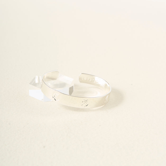 The Darling Effect's "You Are Ambitious" Cuff Bracelet in sterling silver, featuring subtle engravings, rests on a light cream background by a clear geometric accent—an elegant, meaningful gift choice.