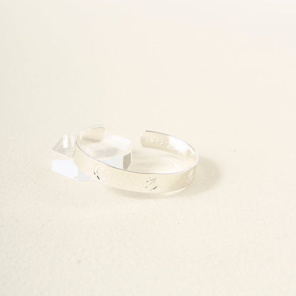 The Darling Effect's "You Are Ambitious" Cuff Bracelet in sterling silver, featuring subtle engravings, rests on a light cream background by a clear geometric accent—an elegant, meaningful gift choice.