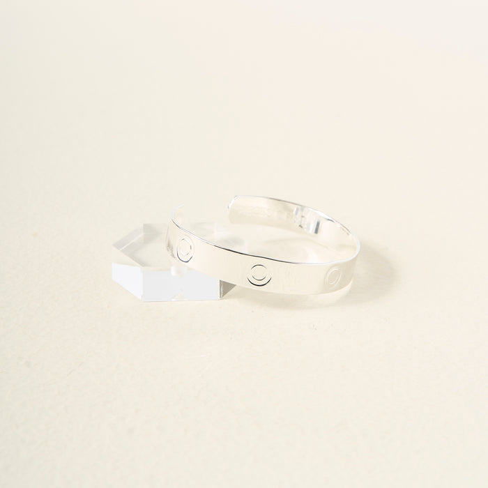 The Darling Effect’s You Are Bold Cuff Bracelet, a sterling silver cuff engraved with circle designs, rests on a light surface beside a clear hexagonal crystal—making it a meaningful gift.