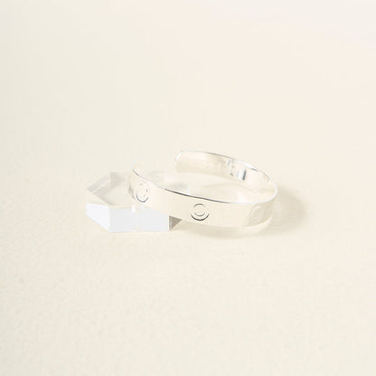 The Darling Effect’s You Are Bold Cuff Bracelet, a sterling silver cuff engraved with circle designs, rests on a light surface beside a clear hexagonal crystal—making it a meaningful gift.