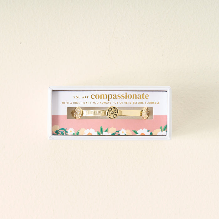 The Darling Effect You Are Compassionate Skinny Stacker Bracelet, a 14k gold plated adjustable cuff with floral designs, is displayed in a box featuring a floral border and card that reads: “You are compassionate. With a kind heart you always put others before yourself.”.