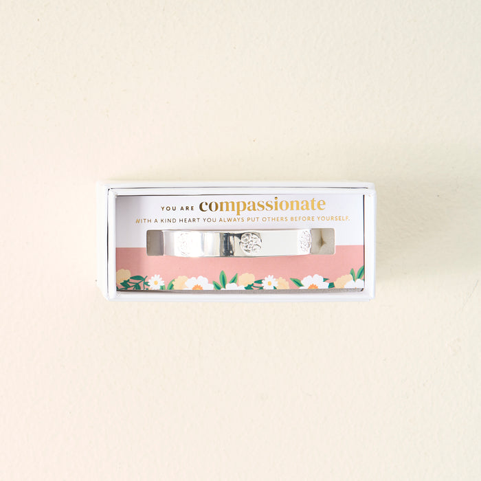 The Darling Effect You Are Compassionate Trait Cuff Bracelet comes in a gift box with a card reading, "You are compassionate. With a kind heart you always put others before yourself," on a pink floral background.