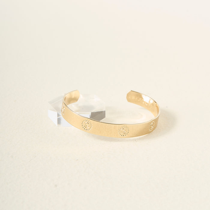 The Darling Effect’s You Are Confident Trait Cuff Bracelet, engraved with a sunburst pattern, rests on a light surface beside a small clear crystal—an ideal meaningful gift for any occasion.