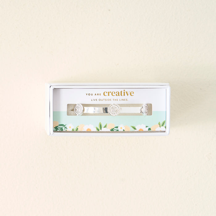 The Darling Effect's "You Are Creative" Skinny Stacker Bracelet is a silver adjustable cuff, gift-boxed with a card reading "You are creative. Live outside the lines." and a floral border—perfect jewelry for any occasion.