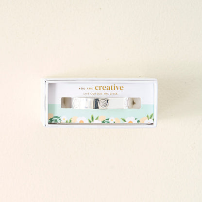 The Darling Effect’s You Are Creative Trait Cuff Bracelet comes in a white floral box that reads “You are creative. Live outside the lines,” making it an inspiring, meaningful gift. Perfect for anyone who values originality.