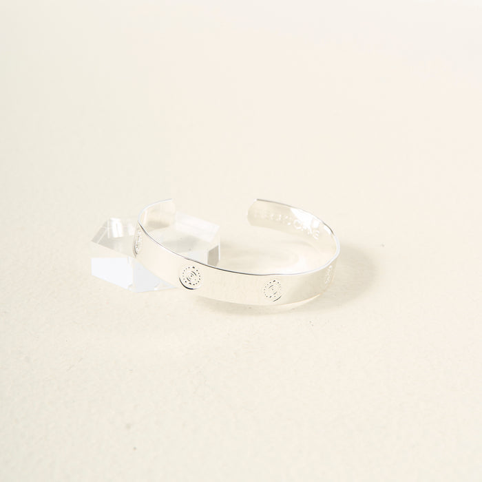 The Darling Effect’s You Are Creative Trait Cuff Bracelet, crafted in sterling silver with small engraved circles, is shown on a textured surface beside a clear acrylic block—a thoughtful gift for any occasion.