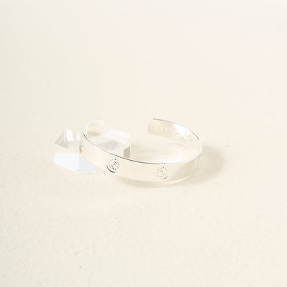 The Darling Effect’s You Are Creative Trait Cuff Bracelet, crafted in sterling silver with small engraved circles, is shown on a textured surface beside a clear acrylic block—a thoughtful gift for any occasion.