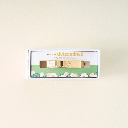 The Darling Effect's You Are Determined Cuff Bracelet comes boxed with the message "You are determined. You can and you will." on green floral packaging, making a meaningful gift set against a light beige background.