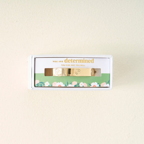 The Darling Effect's You Are Determined Cuff Bracelet comes boxed with the message "You are determined. You can and you will." on green floral packaging, making a meaningful gift set against a light beige background.