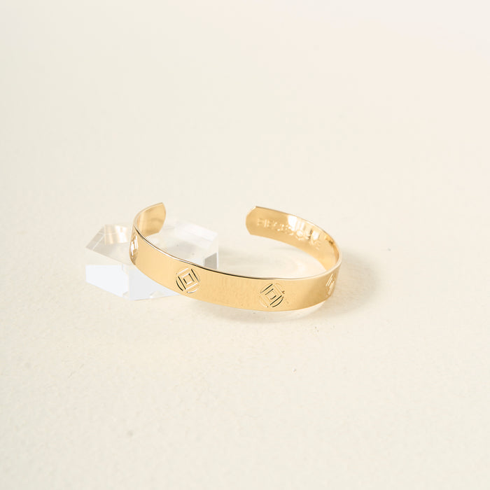 The You Are Determined Cuff Bracelet by The Darling Effect, featuring geometric square engravings, is displayed on a creamy textured surface with clear acrylic blocks—an inspiring gift for any occasion.