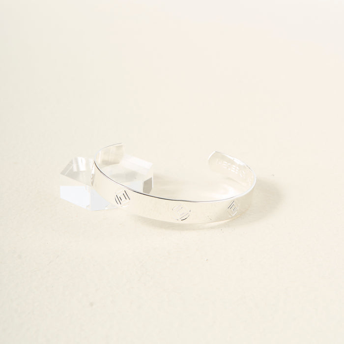 The Darling Effect’s "You Are Determined" cuff bracelet in sterling silver, with engraved lines, rests on a textured surface beside a small crystal—an inspiring and meaningful gift.