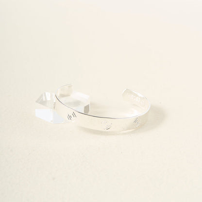The Darling Effect’s "You Are Determined" cuff bracelet in sterling silver, with engraved lines, rests on a textured surface beside a small crystal—an inspiring and meaningful gift.