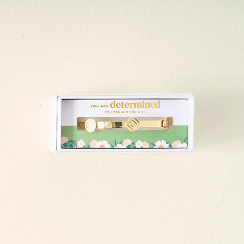 The Darling Effect’s You Are Determined Skinny Stacker Bracelet features two diamond-shaped designs, 14k gold plating, and comes gift-ready in a white box with a floral liner reading “You are determined. You can and you will.”.